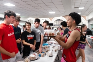 a group of students stand around a table covered in cakes