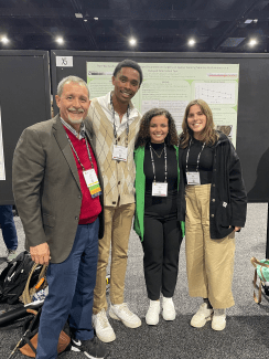 a professor and his three students standing in front of a poster at a conference