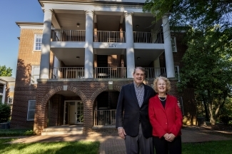 an older couple stands in front of a college residence hall