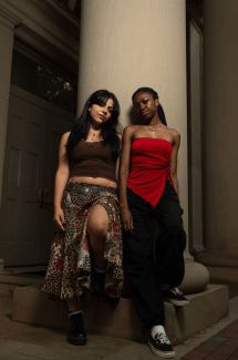 two young women stand leaning against a column