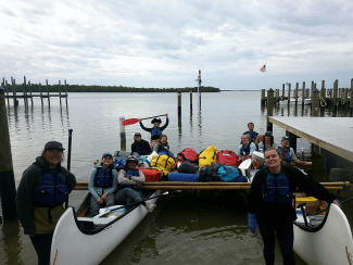 a group of young people smiling while sitting in two canoes in a marina
