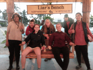a group of young people sit on a hanging bench smiling