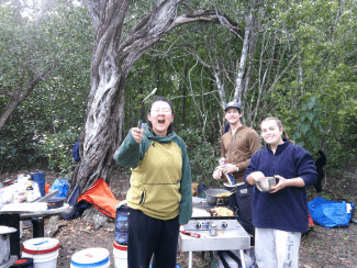 three young people stand together while holding breakfast food at a campsite