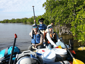 a group of three young people smile from a canoe while wearing sunglasses and hats