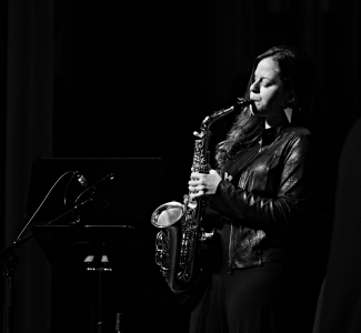 a young woman plays the saxophone on a dark stage