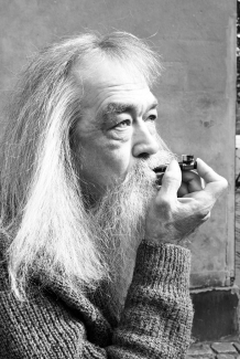a black and white photo of an older man with white hair smoking outside