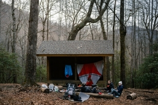 a group of young people sit around a firepit while camping