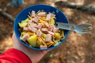 a hand holding a plastic bowl of food in woods