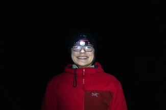 a young white man wearing headlamp and coat at night on hiking trip