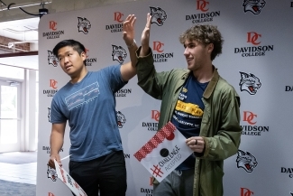 Two students exchange a high five in front of a Davidson College-branded backdrop at All In for Davidson