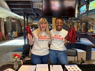 two young women stand together with pom poms wearing "All in for Davidson" tshirts