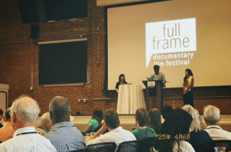 a stage with people talking on it and a screen that reads "Full Frame Documentary Film festival"