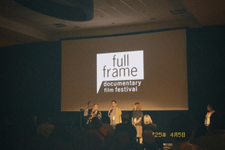 a dark auditorium and a group of three panelists sitting on a stage talking