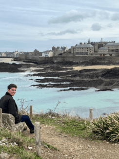 a young white man sits on the bank of a river