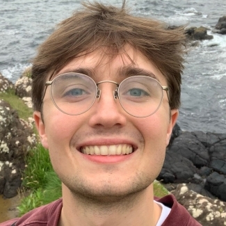 a young white man wearing glasses smiling outside
