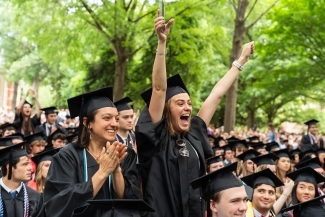 two young women in graduation regalia cheer with their hands in the air