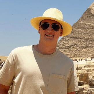 a young man wearing a hat and sunglasses standing in front of an Egyptian pyramid