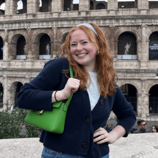 a young white woman with red hair smiling in front of the Rome Colosseum