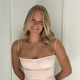a young white woman with blonde hair wearing a pink dress in front of a white wall