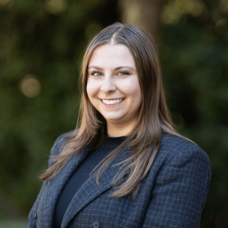 a young white woman with dark hair wearing a blazer and standing outside