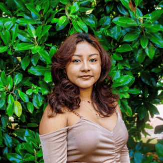 a young woman with dark hair in front of a green bush