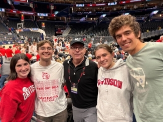 a group of students and Pres. Doug Hicks together in a basketball arena wearing Davidson college gear