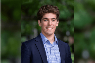 a young white man wearing a collared shirt and jacket with curly brown hair