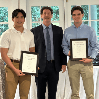 two young men hold awards next to their professor