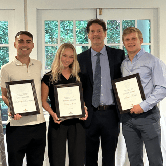 three young students holding awards and smiling with their professor
