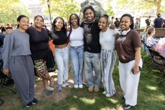 A group of seven smiling students stands together outdoors on a sunny day during a campus event.