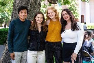 a group of four students smile together in a group outside on a sunny day