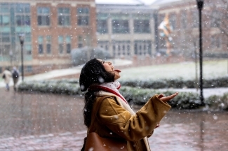 a young woman holds out her tongue to catch a snowflake on a college campus covered with snow