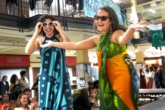 two young women dance in traditional outfits and smile with sunglasses on