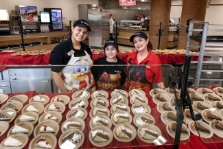 a group of adults in aprons standing behind a table of cake slices