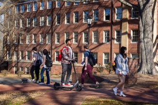 a young Black man rides a scooter past students walking to class on a college campus