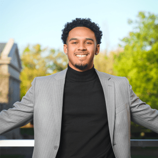 a young Black man wearing a black turtleneck and grey blazer