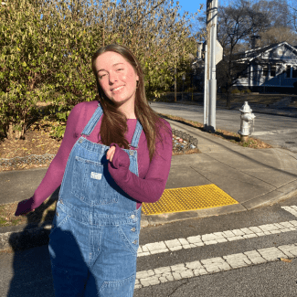 a young woman with long brown hair wearing overalls and a long sleeved shirt on a sunny fall day
