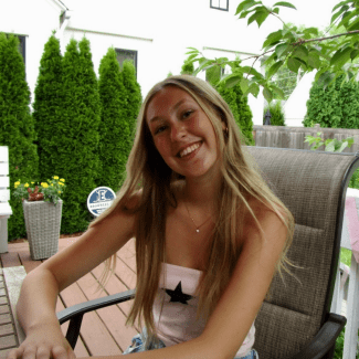a young woman with blonde hair wearing a tube top and sitting on a patio