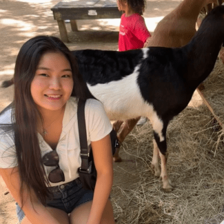 a young woman standing in front of a goat wearing a white tshirt and sunglasses