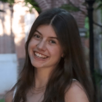 a young woman with long dark hair smiling in front of a brick column