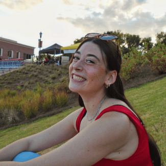 a young woman with dark hair wearing sunglasses and a red top outside