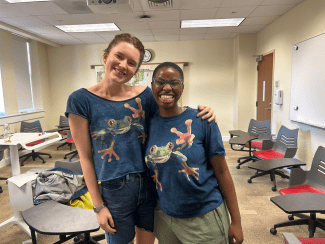 two youn women with matching frog shirts smile together in a classroom