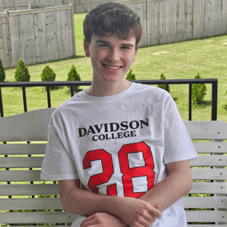 a young man wearing a Davidson College shirt sitting on an outdoor bench