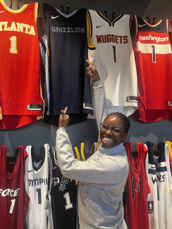 a young Black woman smiles and points at a Grizzlies jersey
