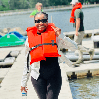a young woman wearing a life jacket on a dock and smiling giving a peace sign