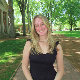 a young woman with blonde hair wearing a black dress on a college campus