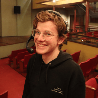 a young man with blonde hair wearing a cap in a theatre with red seats