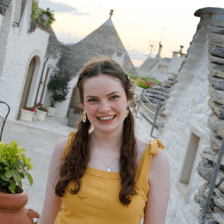 a young woman with curly brown hair in pigtails smiling in a city abroad