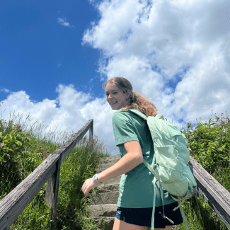 a young woman with blonde hair in a pony tail climbing a staircase outside on a sunny day with a blue sky and clouds in the distance