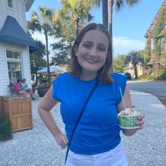 a young woman with short brown hair wearing a blue top and holding a cup of ice cream